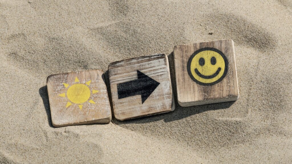 Three wooden blocks with painted images lying on the sand.