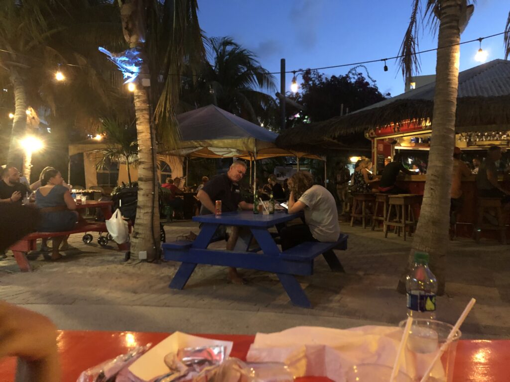 Customers seated at picnic table and open air bar at sunset.