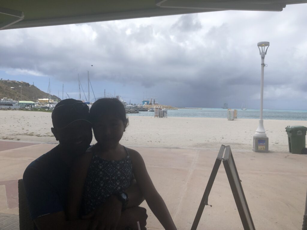 Father and daughter posing for photo with beach in the background.