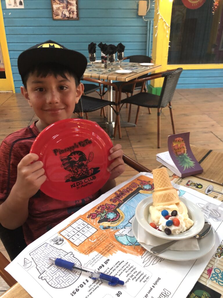 Boy holding Frisbie gift sitting in restaurant with dessert before him.