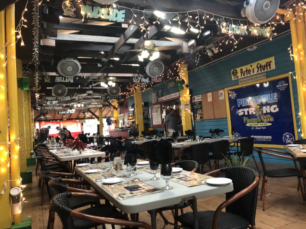 Interior of restaurant set with tables and chairs, and fans and white lights hanging from ceiling.