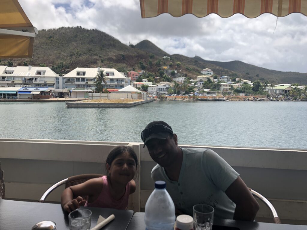 Father and daughter smiling at cafe table overlooking bay.