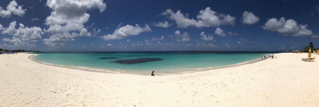 Panoramic view of white sand and turquoise sea with spots of dark coral.