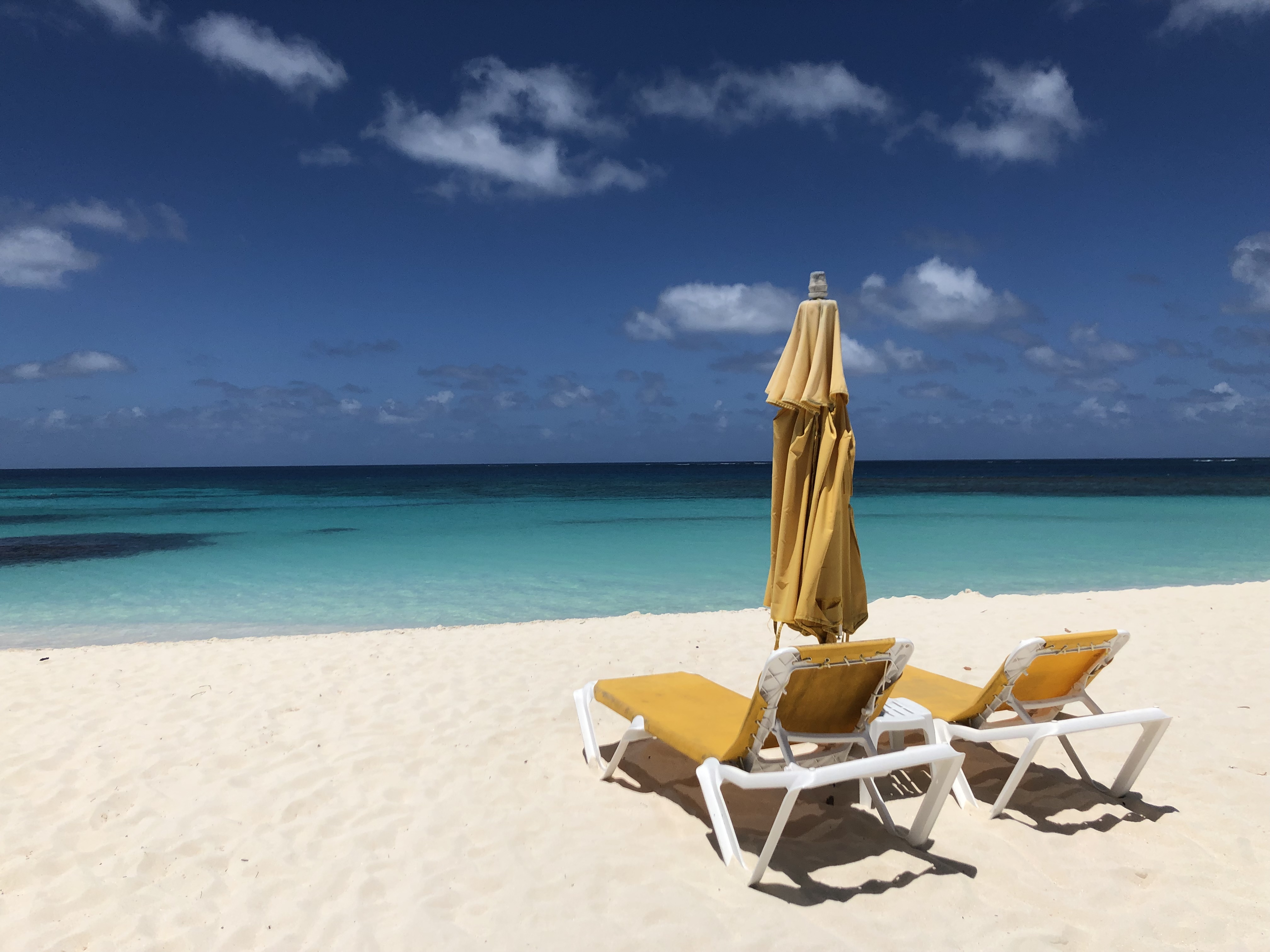 Two beach chairs and umbrella on deserted Caribbean beach.