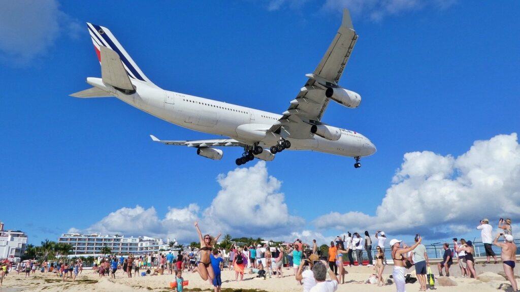 Plane landing over beach filled with people.