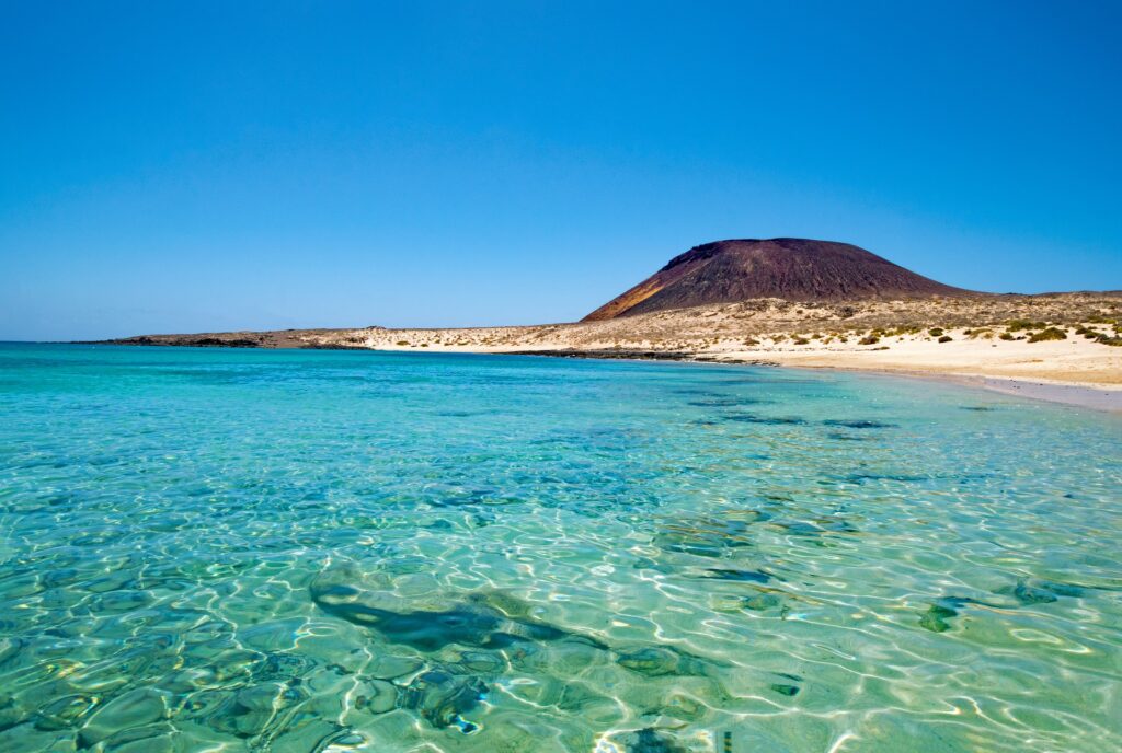 Aqua, shallow water lying along a desert landscape with a hill in the distance.