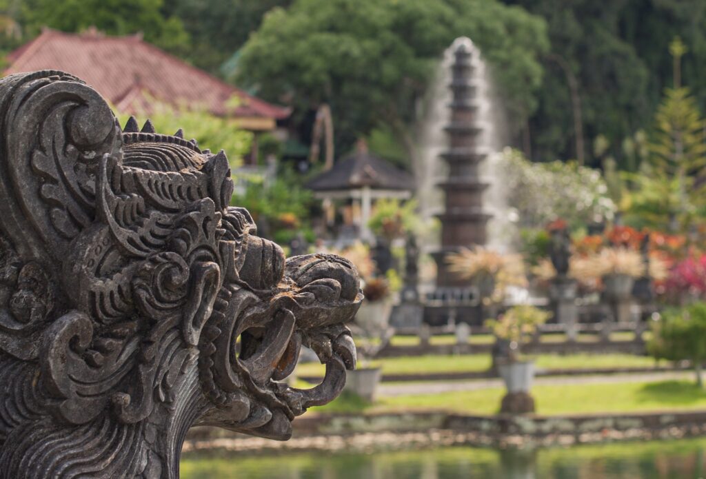 An intricate dragon statue silhouette facing a temple in the travel bucket list country of Bali. 