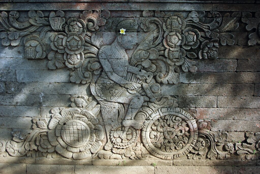 An intricate carving of a man on a bike on the wall of a temple.