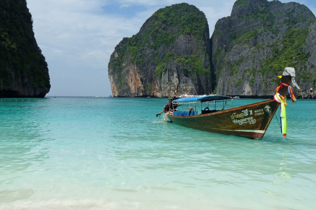 A single traditional boat floating in aqua water in the travel bucket list country of Thailand.