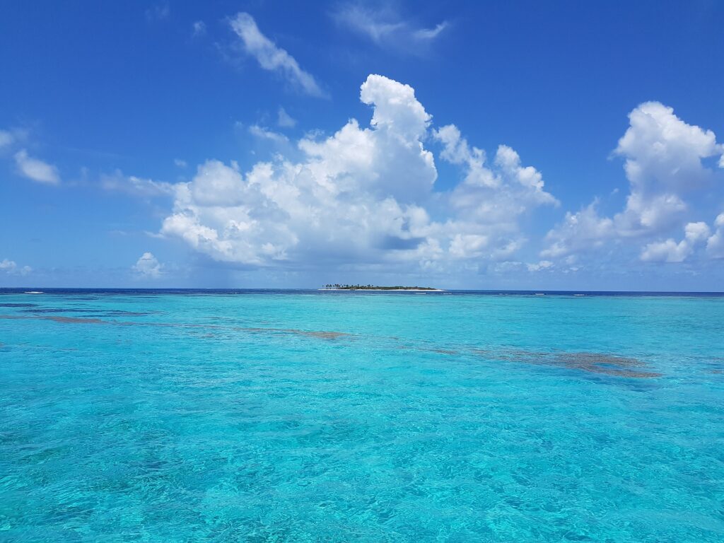 Turquoise, sparkling water stretching to cobalt blue ocean with a tiny island in the distance.