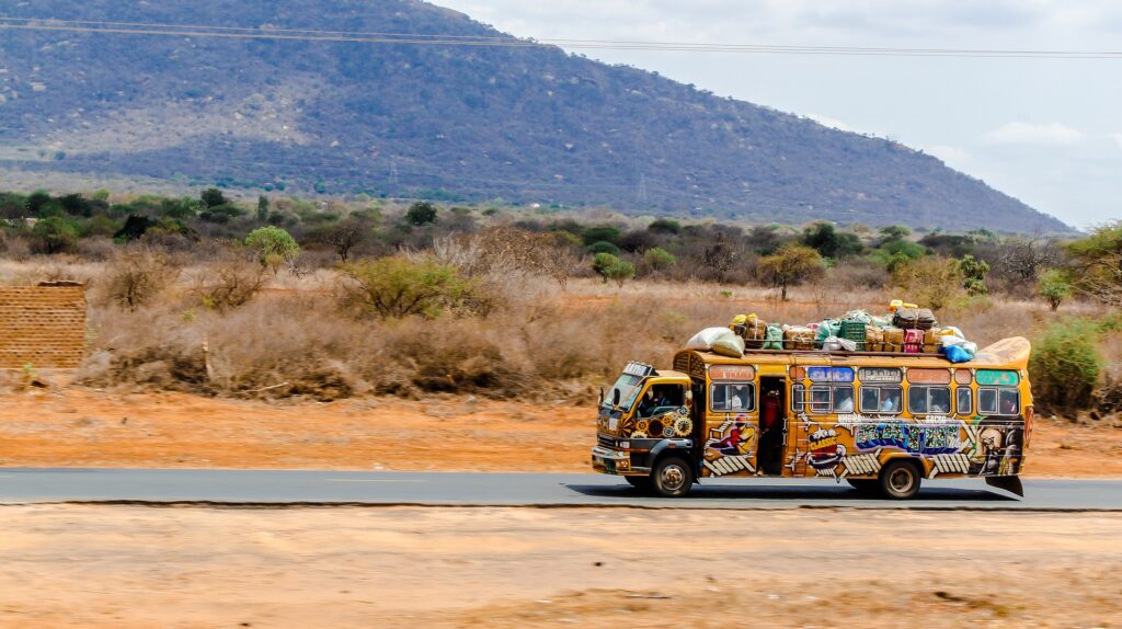 Colorful bus loaded with luggage on roof driving through African countryside.