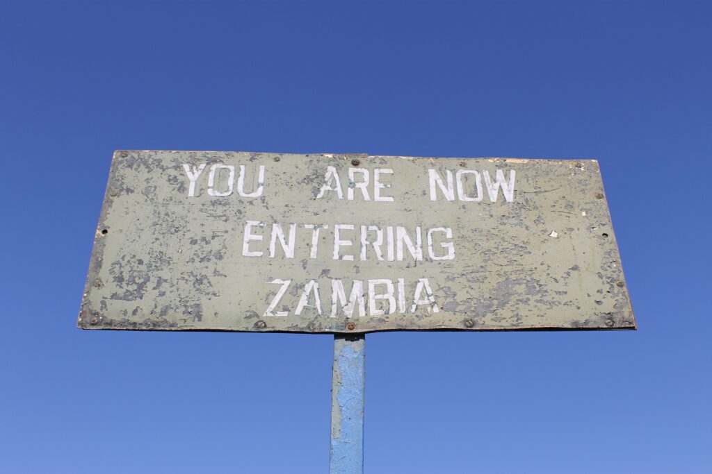 Metal roadside sign reading 'You Are Now Entering Zambia.'