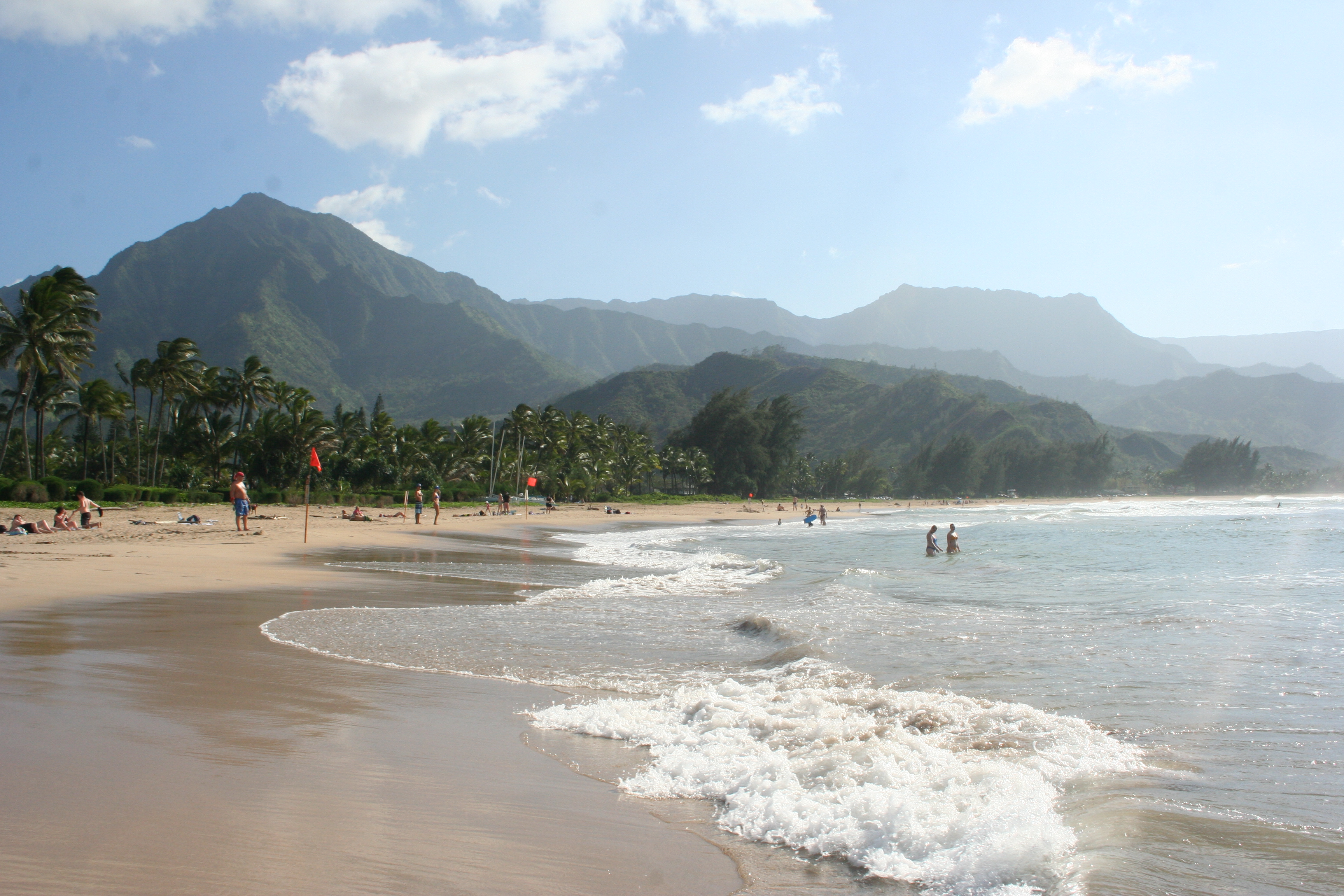 Golden sand with ocean washing up upon it and green mountains in distance.