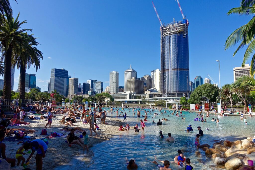 Swimmers swimming in lagoon style pool surrounded by city buildings.