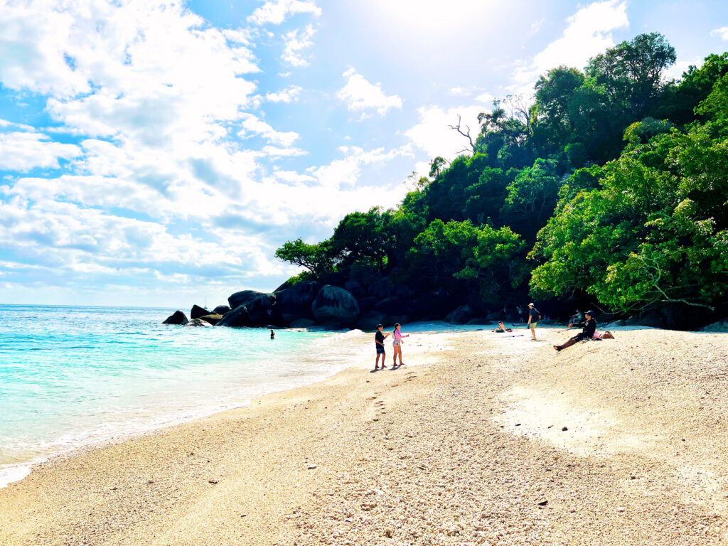 Turquoise and deep blue sea washing onto sand with green hills in distance.