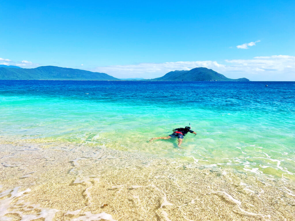 Boy snorkeling on shoreline with turquoise and deep blue sea behind him.