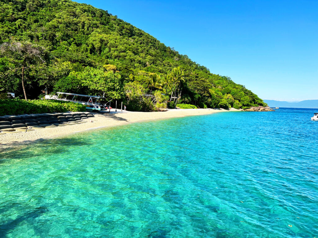 Turquoise sea against a narrow beach leading up into hilly green rainforest.