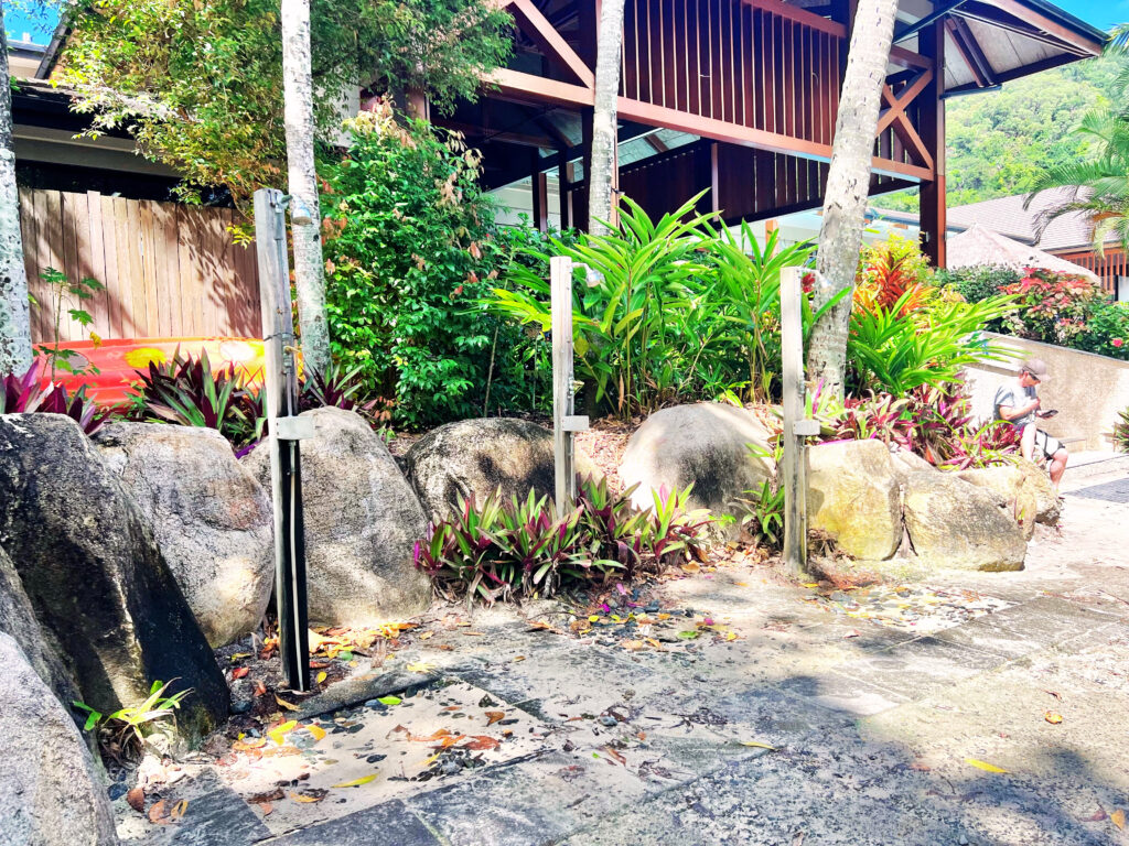 Outdoor showers next boulders and trees beside a building.