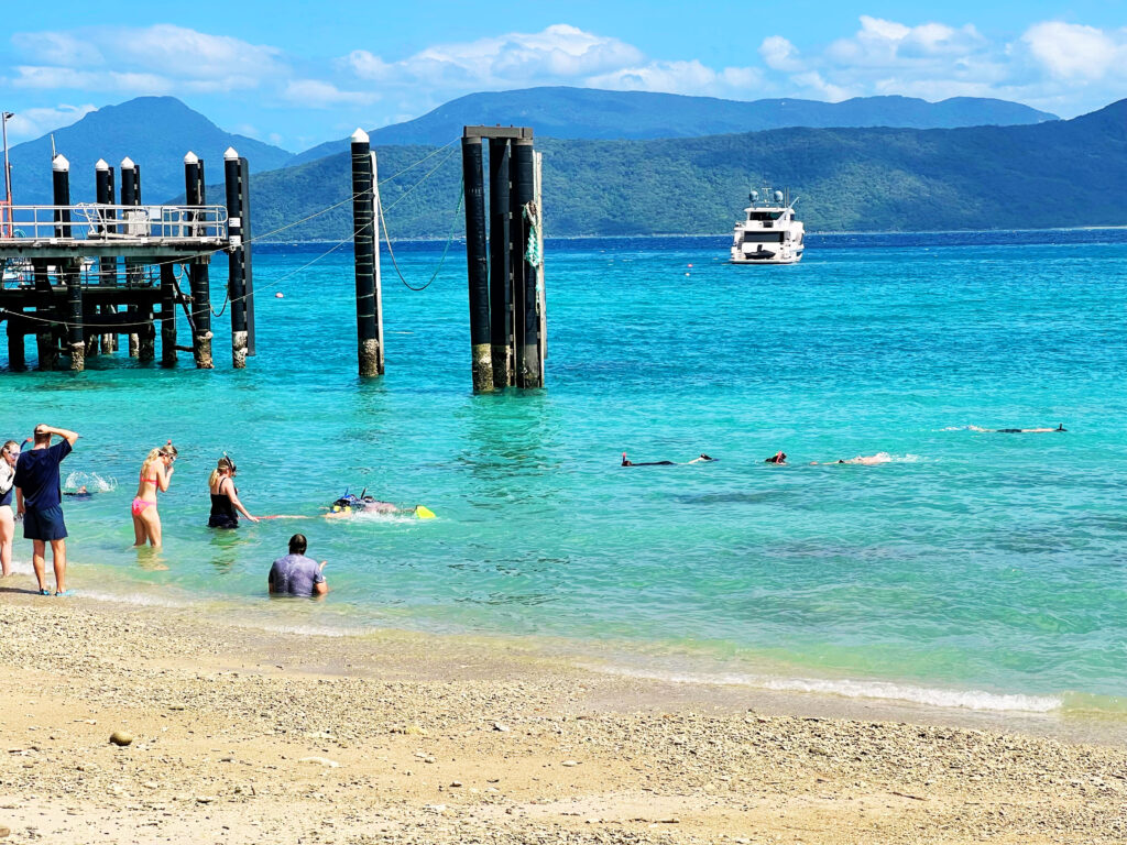 People snorkeling in turquoise water off beach near a dock.