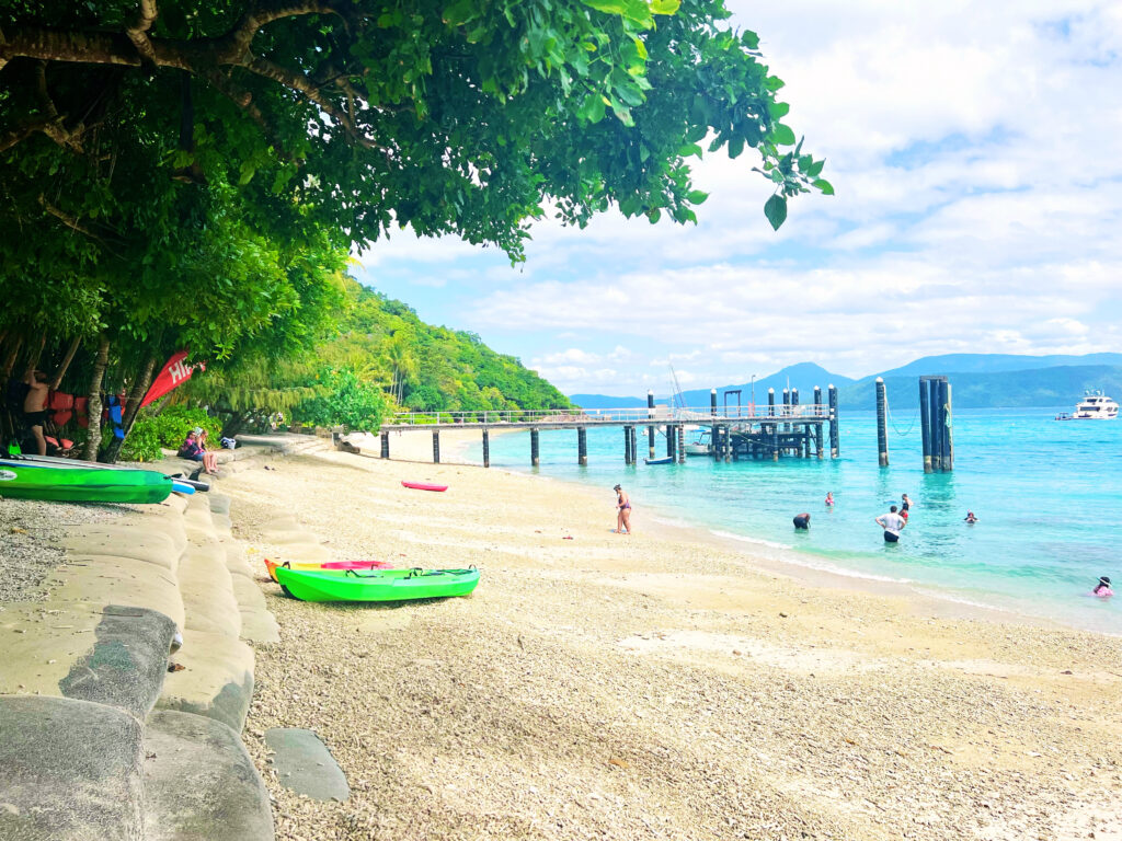 People snorkeling in turquoise water off beach near a dock.