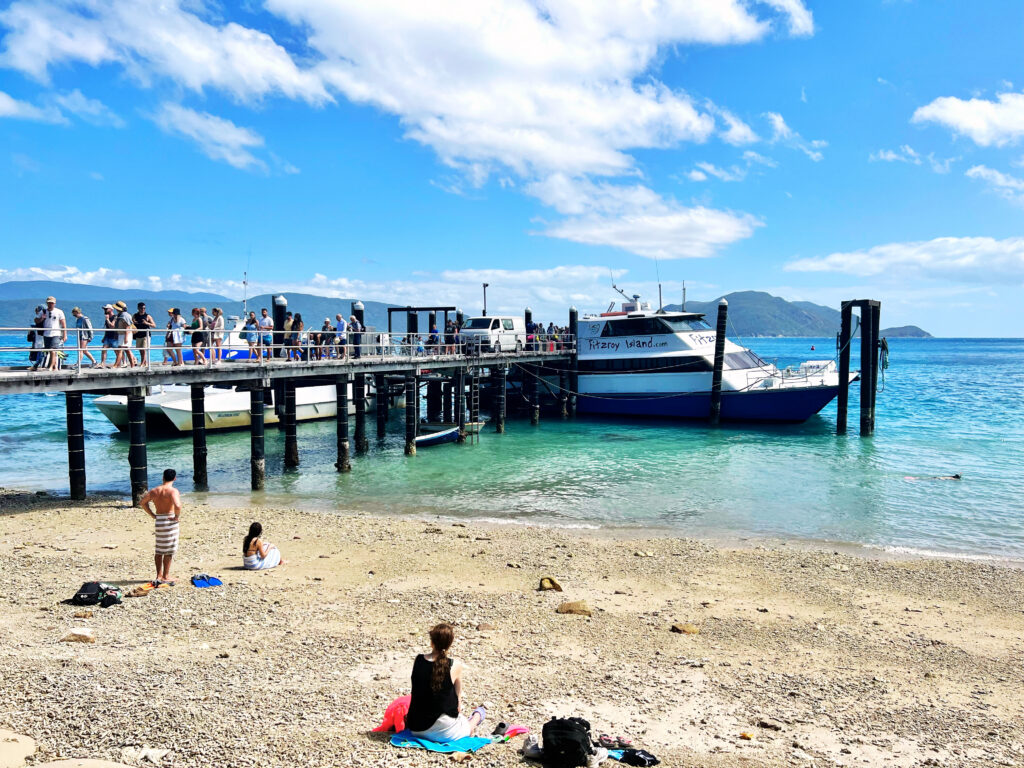 Passengers debarking from a ferry walking down a dock while people watch from beach.