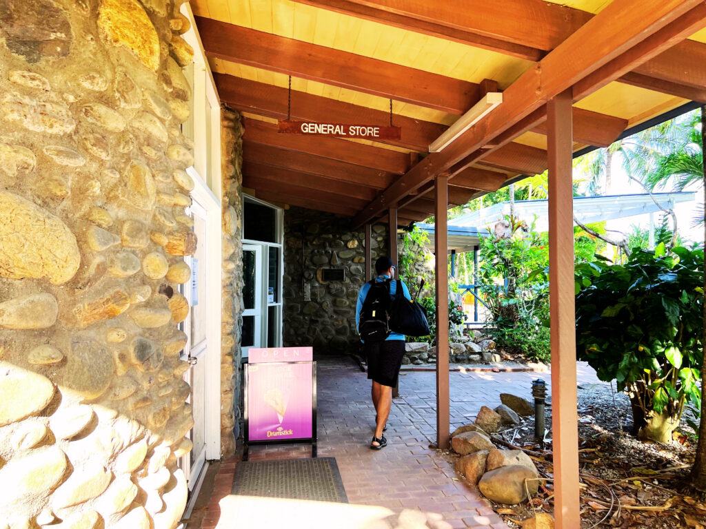 Man walking along brick path beneath wooden roof next to stone building.