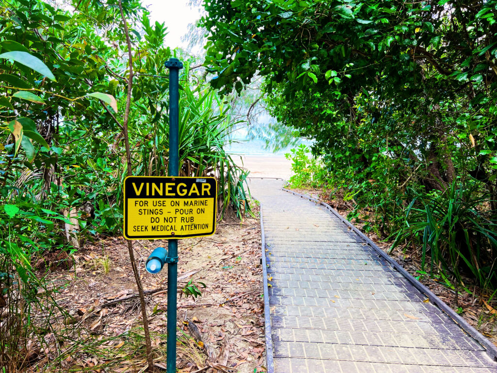 Sign on post next to boardwalk in rainforest leading to the beach.