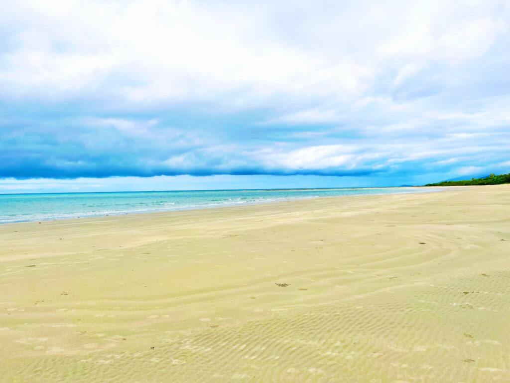 Beach in foreground with aqua sea in background beneath heavy clouds.