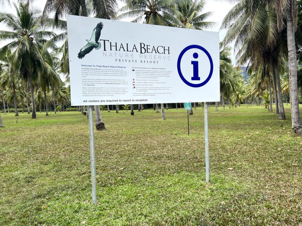 White sign for Thala Beach Nature Reserve in ground with palm trees in background, a stop on your 5 days in Tropical North Queensland trip.