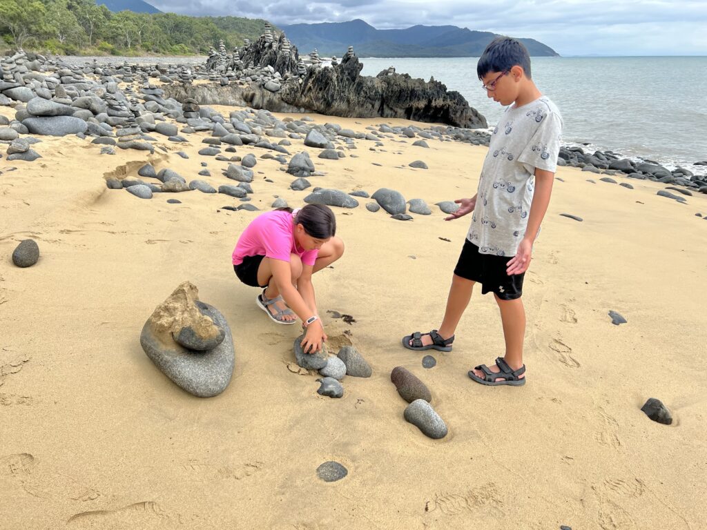 Children stacking rocks into sculptures on beach next to sea.