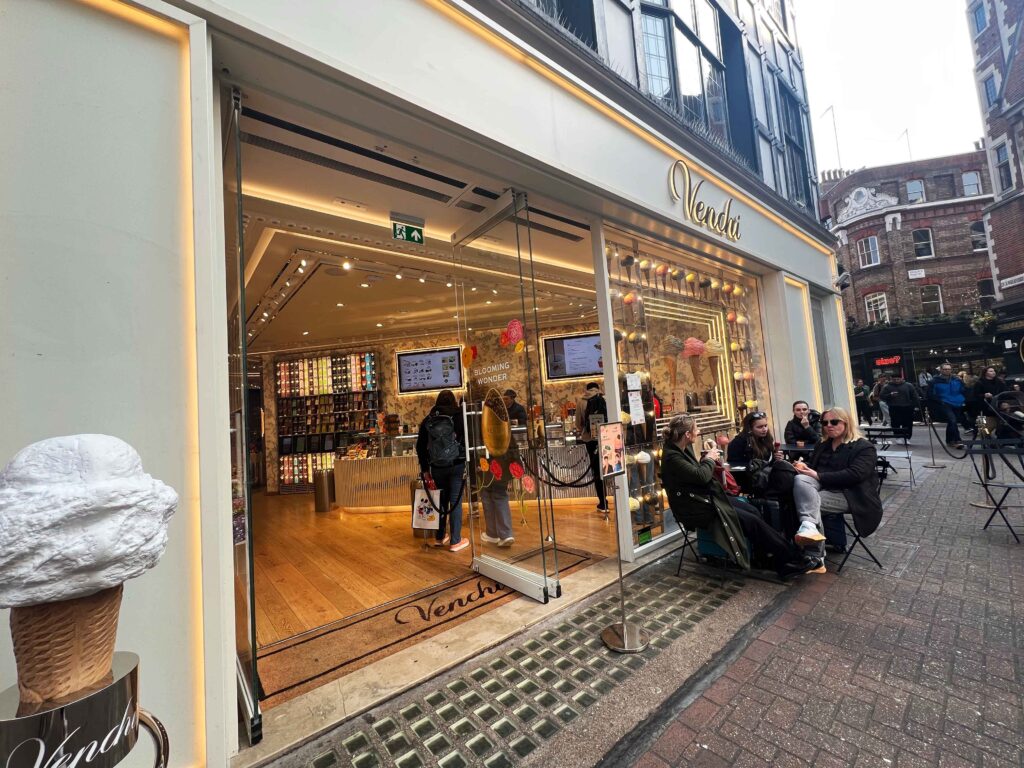 Shop front for an ice cream store with customers eating at tables out front.