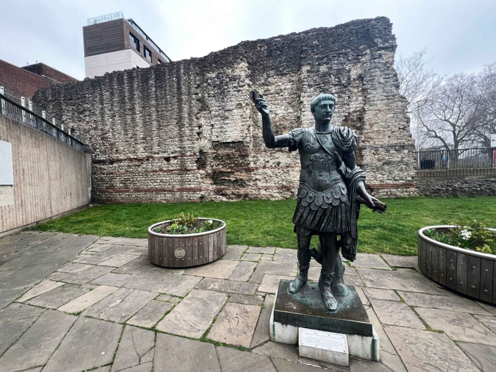 Roman statue posed before a section of ancient Roman wall.
