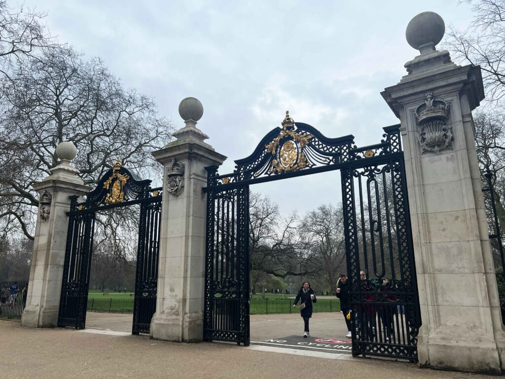 An intricate metal and gold gate set between concrete pillars leading to a park.