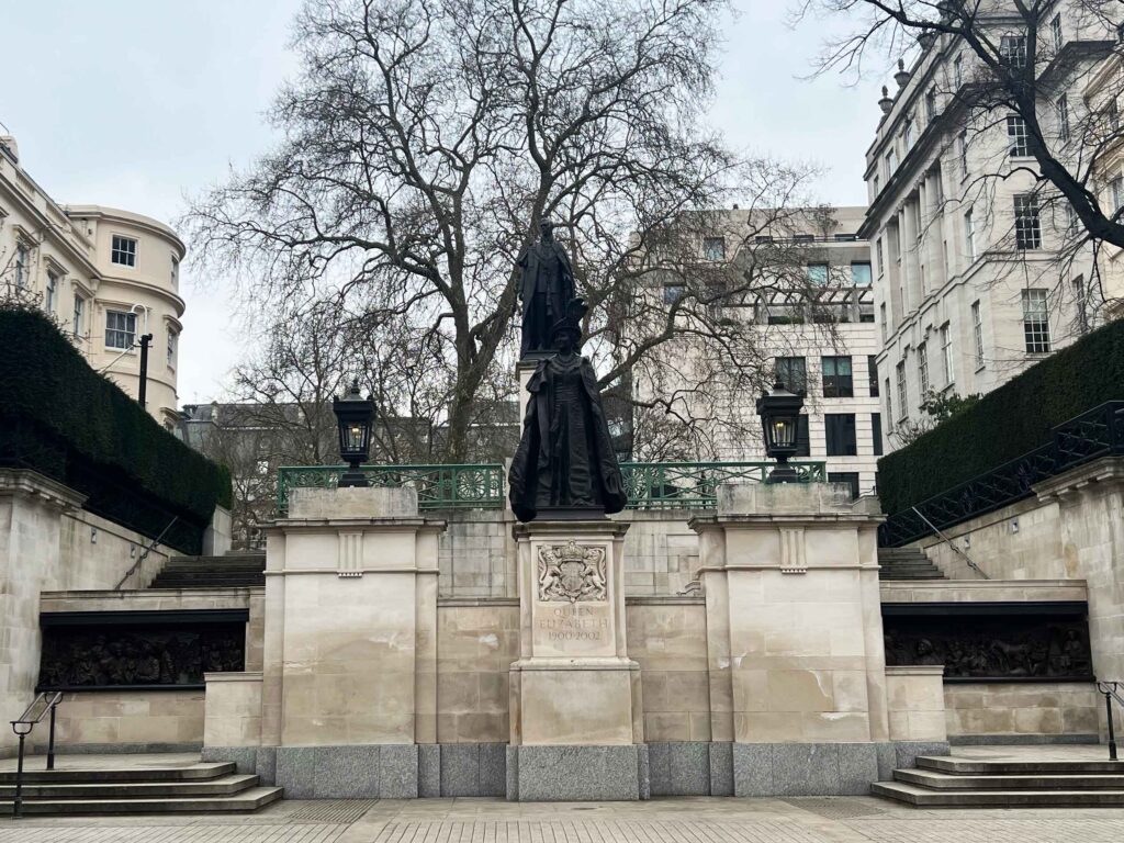 Looking towards two statues of royalty on monuments on a street in London.