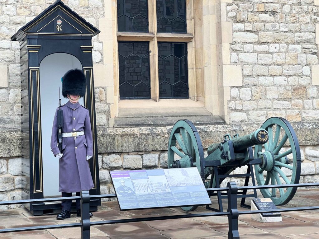 A soldier in blue with black headdress standing outside a stone building.