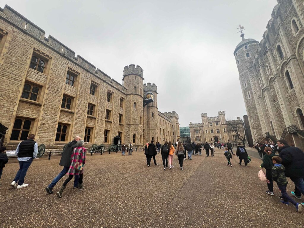 People walking between tall stone buildings in the Tower of London.