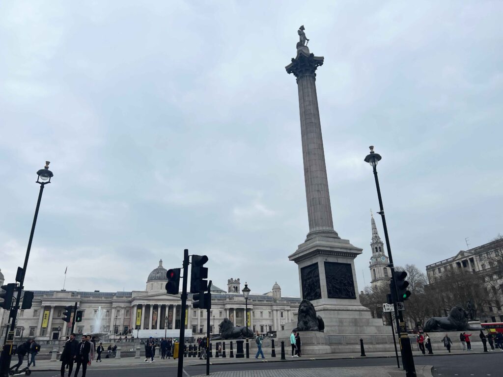 Looking across Trafalgar square with a statue atop a tall pillar monument.
