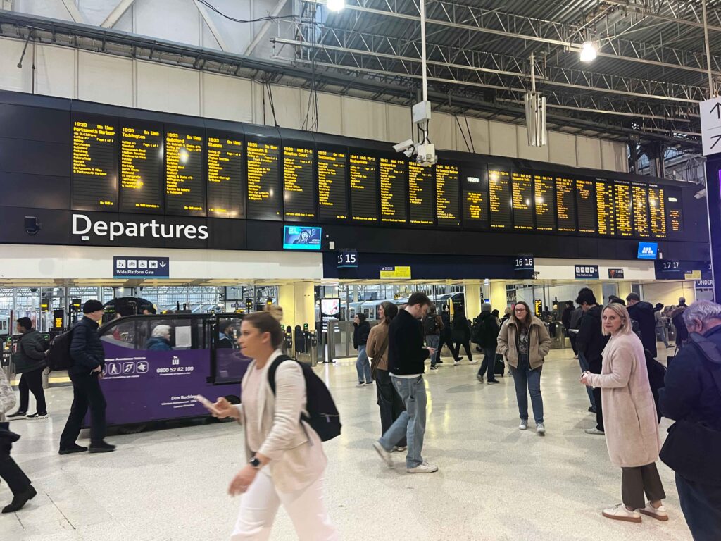 Departures board mounted above walking passengers inside a train building.