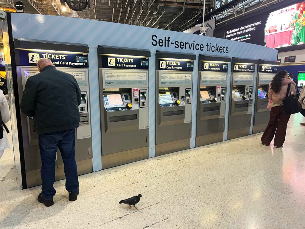 Self-service ticket kiosks lined up in a row inside a train station.