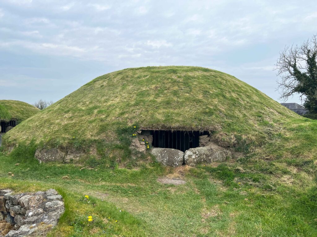 Grass covered mound with metal bars blocking entrance to inner cave.