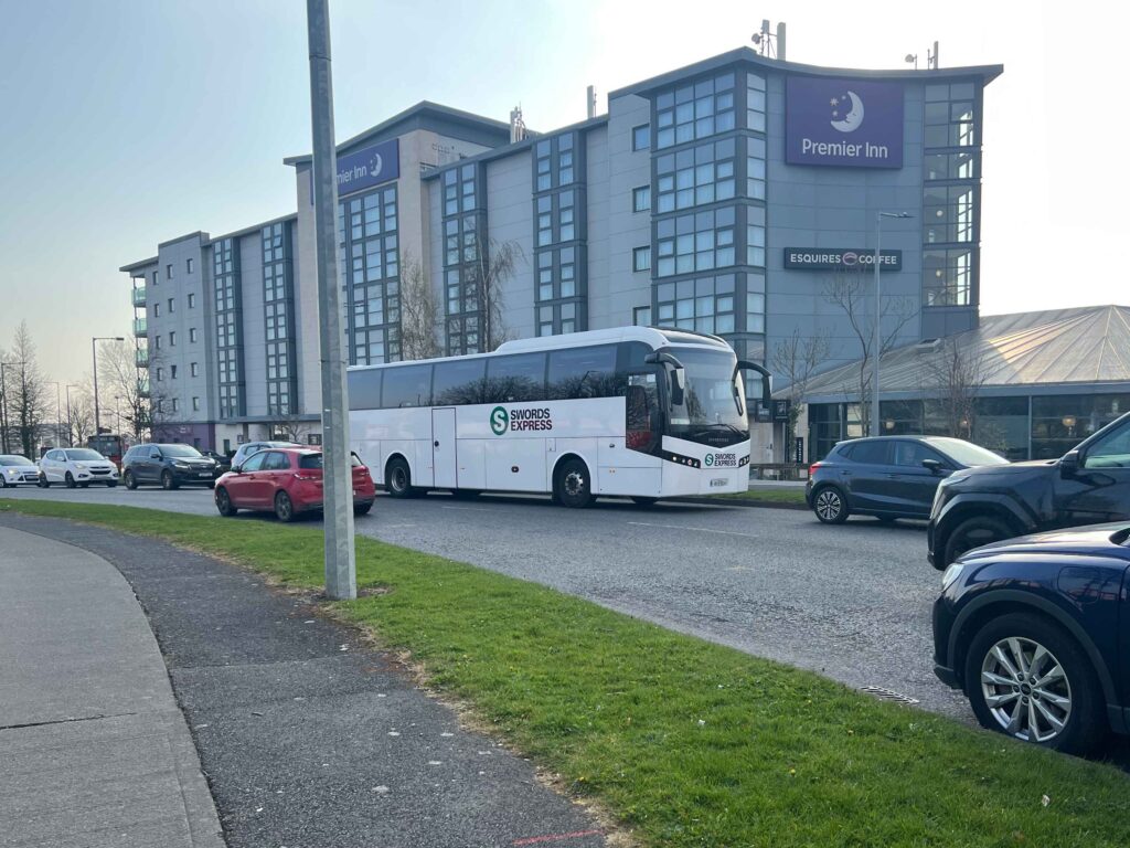 Large white bus driving by hotel.