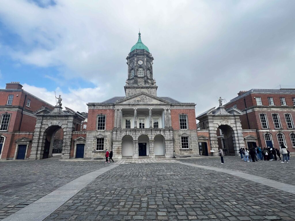 Old bell tower above a red brick and concrete building before a cobbled square.