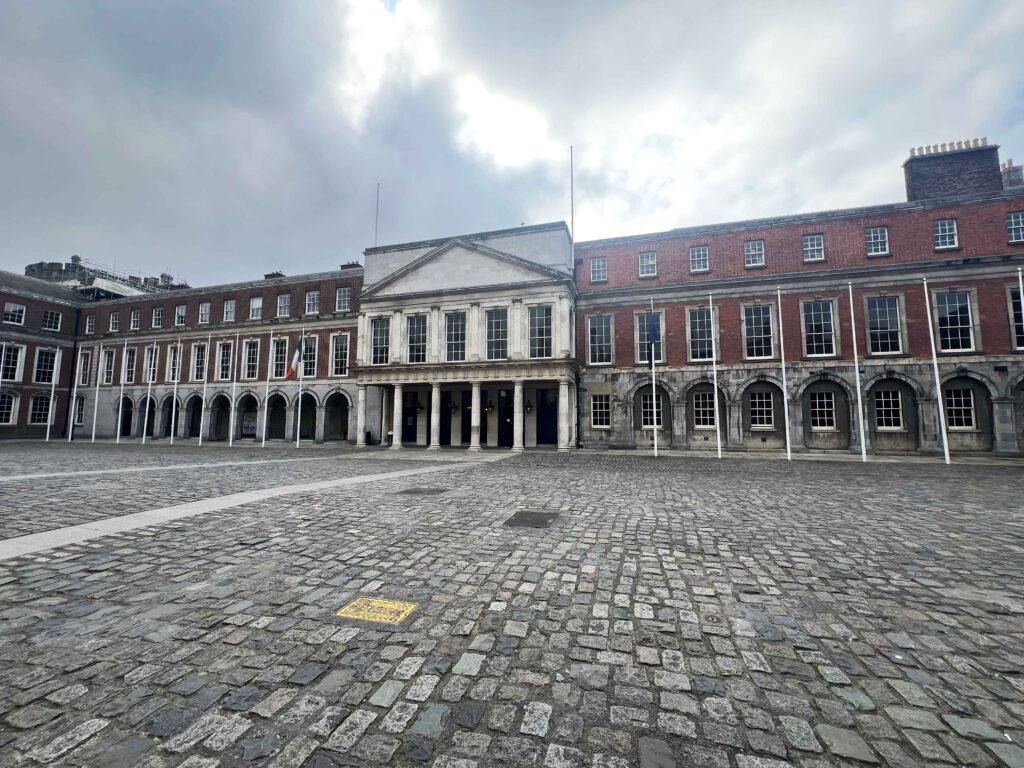 Stately building in red brick and concrete with cobbled square before it.