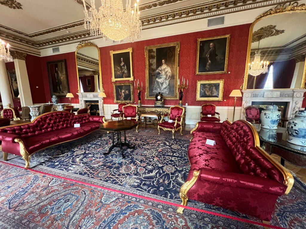 Ornate red velvet furniture set before a wall displaying gold framed old paintings.