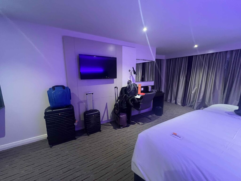 A tv mounted on a wall in a hotel room with luggage beneath.