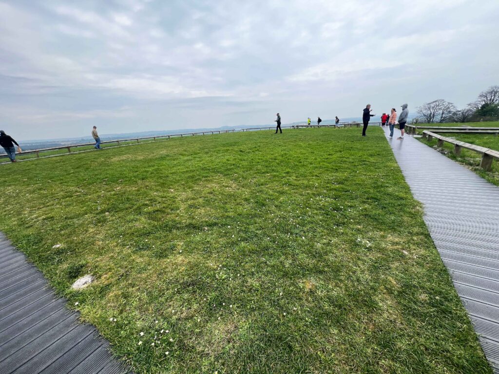 Grassy knoll with people walking on a pathway around it.