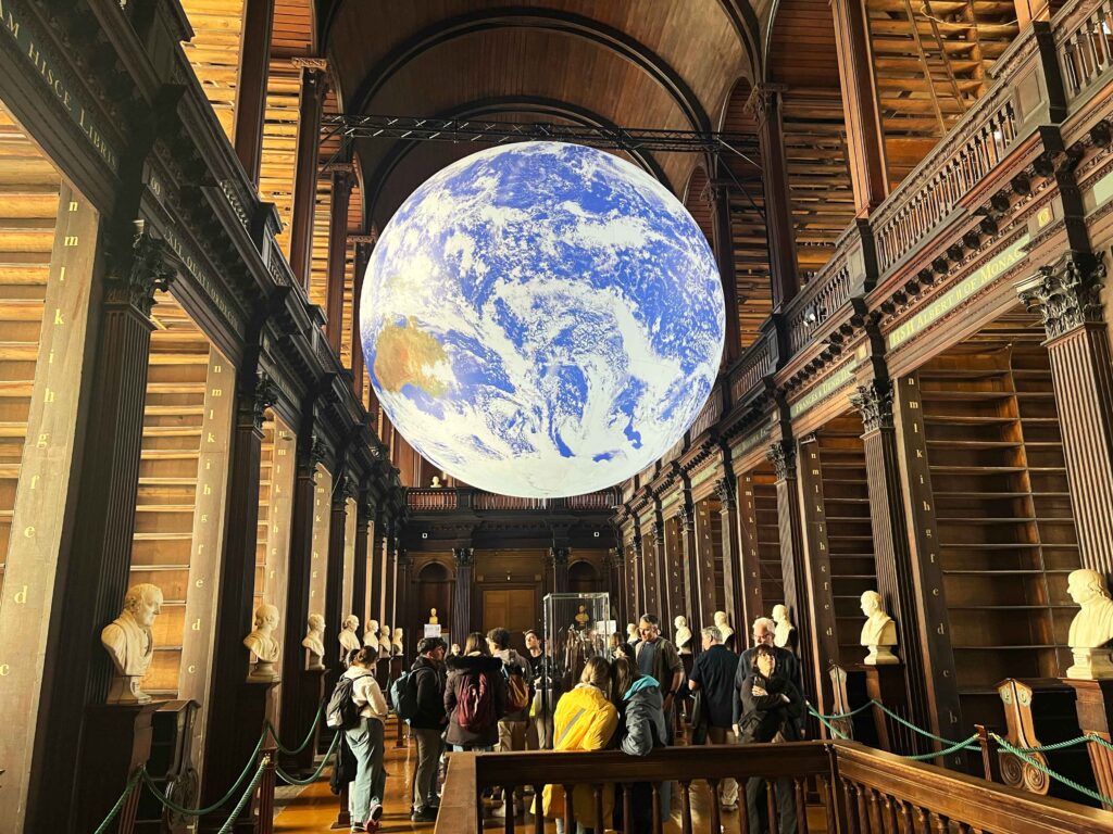 An illuminated digital earth suspended in air in a historic library.