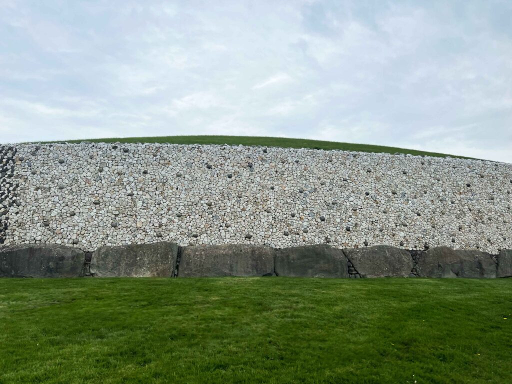 Large stone wall with boulders at the bottom and grassy mound top.