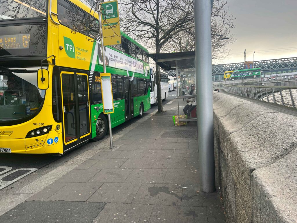 Green and yellow bus parked next to a bus stop where you can catch a city bus on a stopover in Ireland.