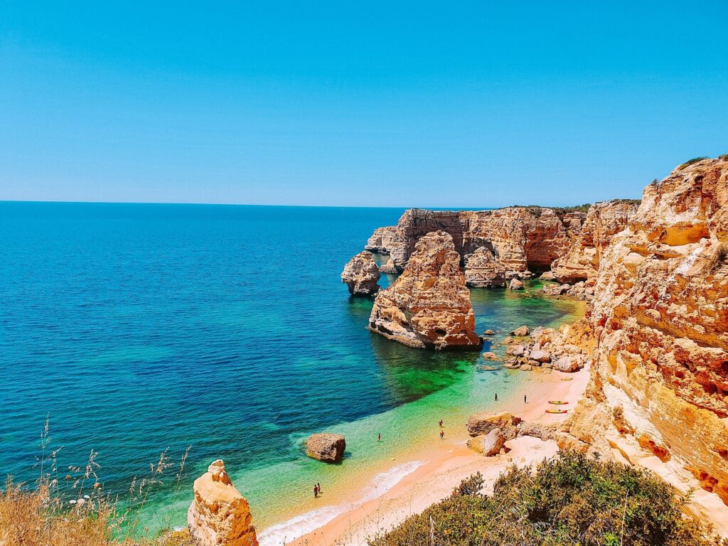 Rust colored rocky cliffs lining a narrow beach next to the sea.